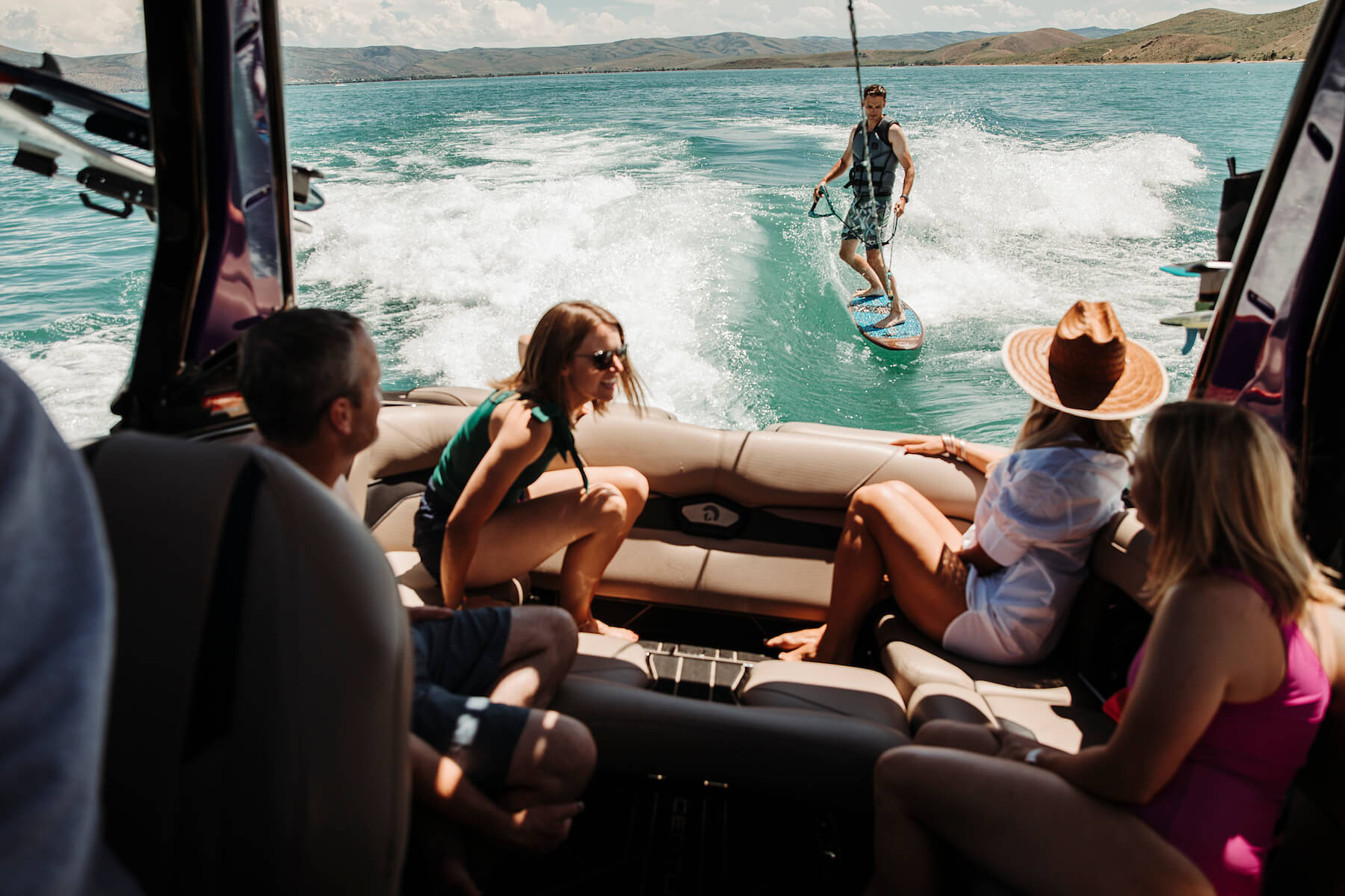 group talking on boat while man surfs behind boat